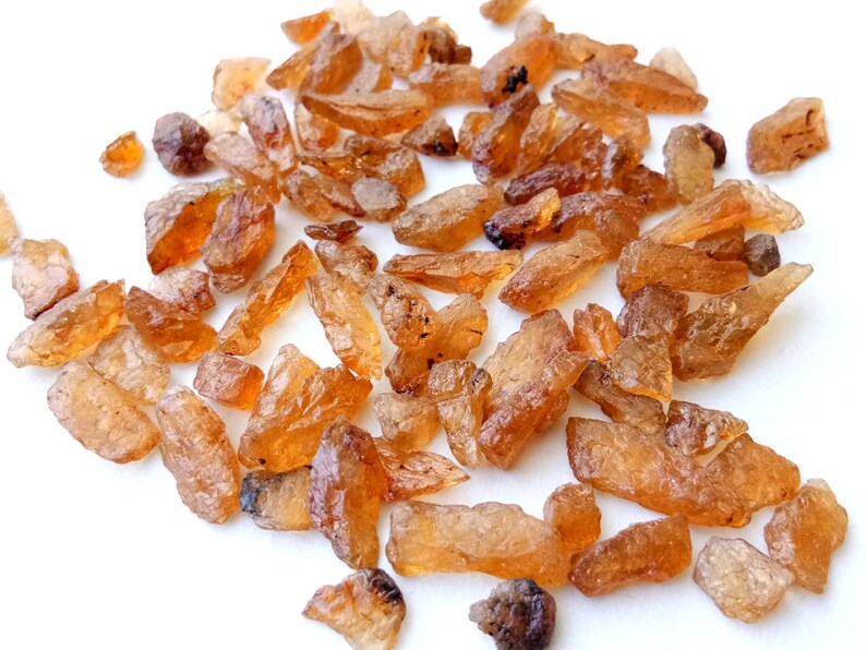 May include: A collection of small, rough, orange-brown gemstones. The stones are irregularly shaped and have a translucent appearance.