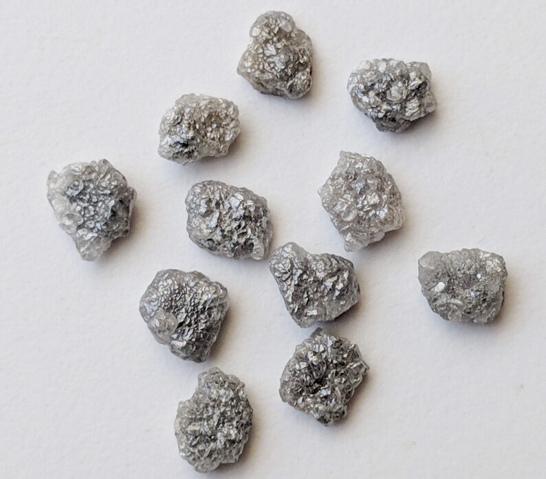 K&ouml;nnte beinhalten: Eine Sammlung von zehn rohen, grauen Diamanten. Die Diamanten sind in verschiedenen Gr&ouml;&szlig;en und Formen, mit einer rauen, unpolierten Oberfl&auml;che.