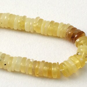 May include: A strand of yellow opal beads, each bead is a stack of thin, round slices. The beads are strung on a clear thread.