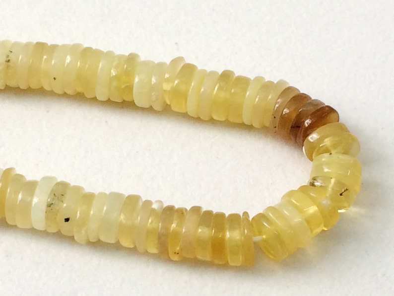 May include: A strand of yellow opal beads, each bead is a stack of thin, round slices. The beads are strung on a clear thread.