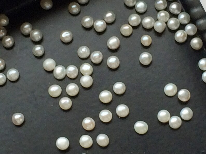 May include: A collection of white pearls scattered on a black surface. The pearls are of various sizes and shapes.