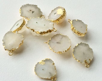 May include: A collection of eight white agate gemstone pendants with gold-plated edges. The pendants are irregular in shape and have a natural, raw look.