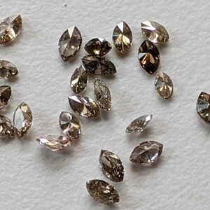 Puede incluir: Una colecci&oacute;n de 20 diamantes marrones en forma de marquesa, esparcidos sobre una superficie blanca.