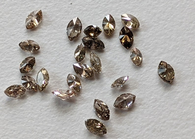 Puede incluir: Una colecci&oacute;n de 20 diamantes marrones en forma de marquesa, esparcidos sobre una superficie blanca.