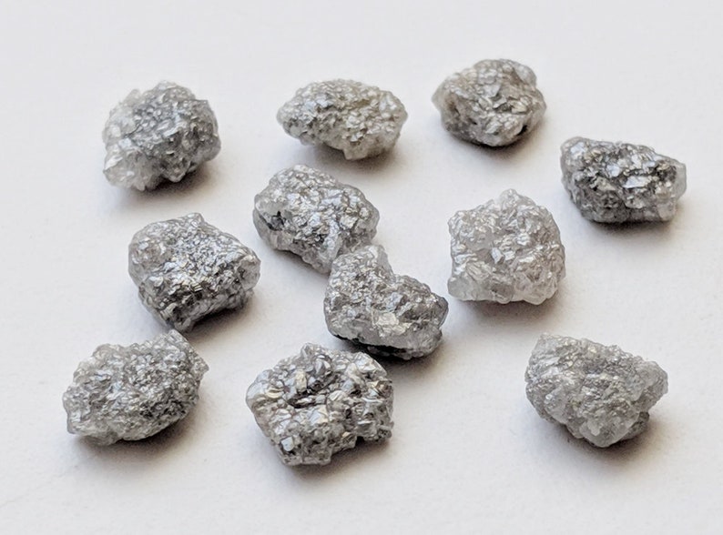 K&ouml;nnte beinhalten: Eine Sammlung von zehn rohen, grauen Diamanten. Die Diamanten haben verschiedene Formen und Gr&ouml;&szlig;en und haben ein nat&uuml;rliches, unpoliertes Aussehen.