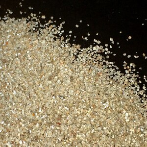 May include: A pile of small, clear, and sparkly crystals on a black background. The crystals are various sizes and shapes, and they are scattered across the surface.