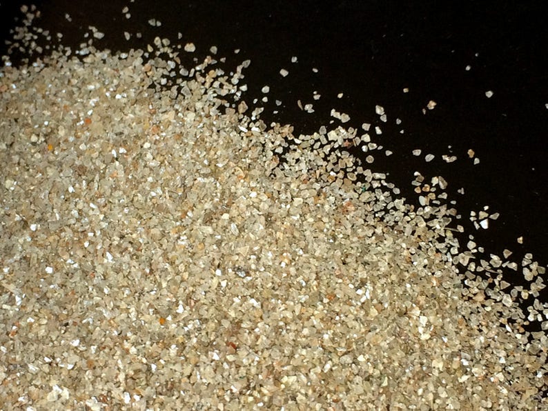 May include: A pile of small, clear, and sparkly crystals on a black background. The crystals are various sizes and shapes, and they are scattered across the surface.