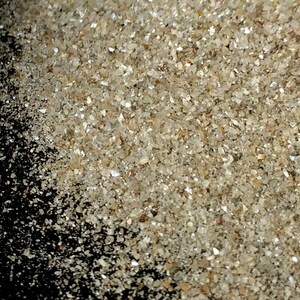 May include: A close-up of a pile of small, clear, and white crystals. The crystals are scattered on a black surface.