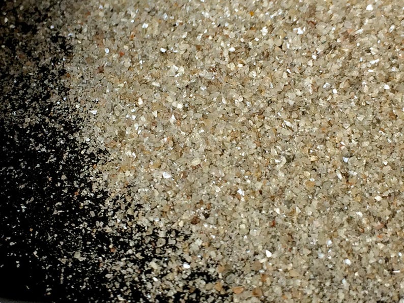 May include: A close-up of a pile of small, clear, and white crystals. The crystals are scattered on a black surface.