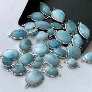 May include: A collection of oval-shaped, light blue gemstone beads with silver-toned metal accents. The beads have a cloudy, iridescent appearance.