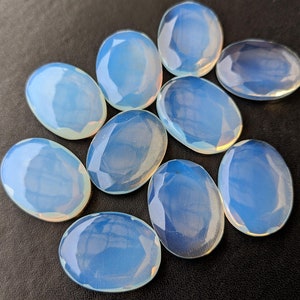May include: Ten oval-shaped, polished, iridescent opal stones. The stones are a pale blue color with a white, opalescent sheen.