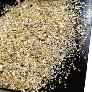 May include: A pile of gold and silver glitter on a black surface. The glitter is made up of small, irregular pieces.