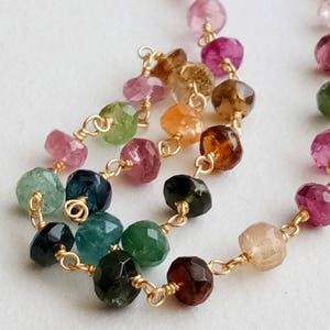 Peut inclure: Un collier en chaîne dorée avec des pierres précieuses facettées de différentes couleurs, notamment rose, vert, bleu et marron. Les pierres précieuses sont reliées par de petites attaches en fil d'or.