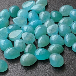 May include: A collection of numerous loose, teardrop-shaped gemstones in a vibrant turquoise-blue color. Each stone features a smooth, polished, and rounded cabochon surface that reflects light, showcasing a consistent semi-translucent appearance.