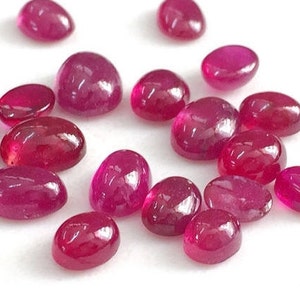 May include: A collection of oval-shaped, cabochon cut, ruby gemstones. The rubies are a deep red color and have a smooth, polished finish.