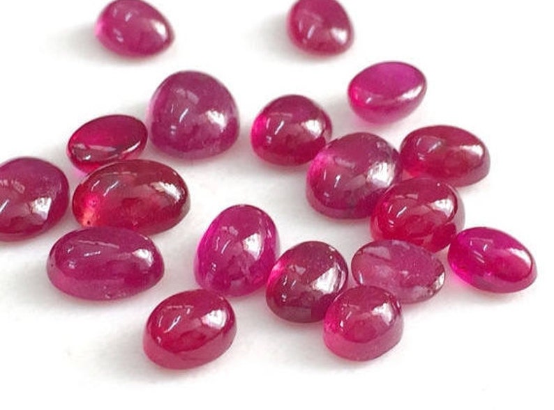 May include: A collection of oval-shaped, cabochon cut, ruby gemstones. The rubies are a deep red color and have a smooth, polished finish.