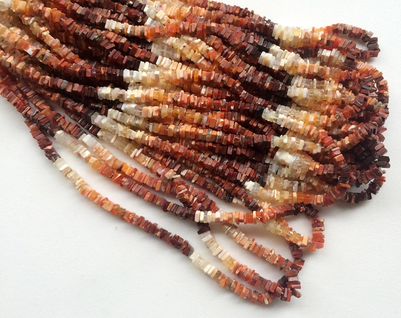 May include: A strand of red, orange, and white gemstone beads. The beads are square and have a rough, natural finish.