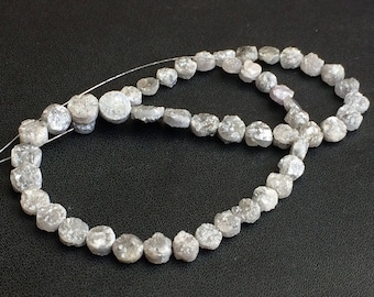 Könnte beinhalten: Eine Kette aus rohen Diamantperlen in verschiedenen Formen und Größen. Die Perlen sind überwiegend grau mit einer leicht rauen Textur und auf einer dünnen, weißen Schnur aufgefädelt. Die Perlen haben einen Durchmesser von ca. 0,5 cm bis 1 cm.