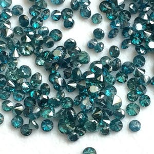 May include: A collection of loose blue diamonds, scattered on a white surface. The diamonds are faceted and have a dark blue colour.