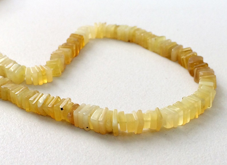 May include: A strand of yellow opal beads, each bead is a rectangular shape with a slightly irregular, faceted surface.