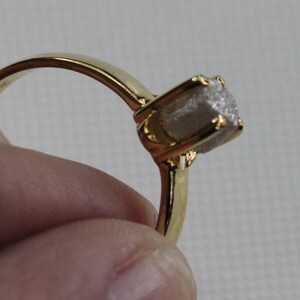 May include: A gold ring with a rough, white diamond-shaped stone set in the centre.