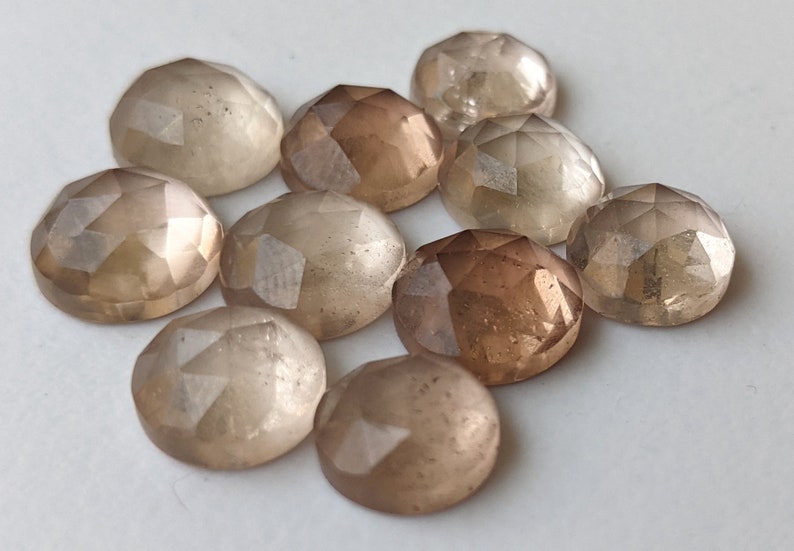 Puede incluir: Diez cabujones de piedra preciosa facetados en tonos de marr&oacute;n claro y beige. Las piedras son redondas y tienen un acabado liso y pulido.