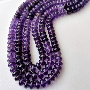 May include: A strand of purple amethyst beads, each bead is round and faceted. The beads are strung on a clear thread and are arranged in a loose, flowing pattern.