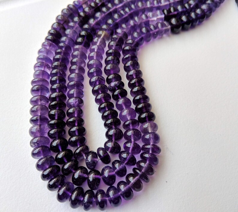 May include: A strand of purple amethyst beads, each bead is round and faceted. The beads are strung on a clear thread and are arranged in a loose, flowing pattern.