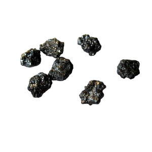 May include: A collection of seven small, black, irregularly shaped stones. The stones have a rough, textured surface.