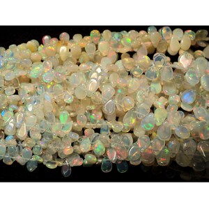 May include: A strand of white opal gemstone beads in a teardrop shape. The beads are translucent and have a rainbow iridescent sheen.