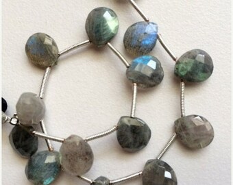 May include: A strand of silver beads with faceted, teardrop-shaped labradorite gemstones. The stones are a mix of grey, green, and blue with iridescent flashes.