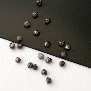 May include: A collection of small, black, rough diamonds on a white and black surface.
