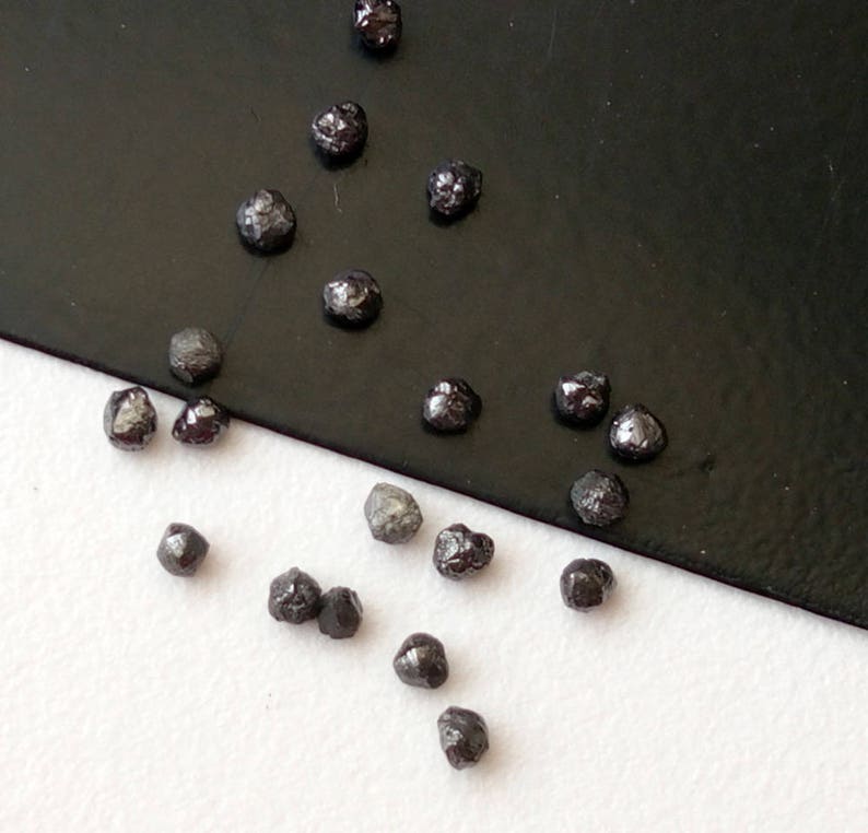 May include: A collection of small, black, rough diamonds on a white and black surface.