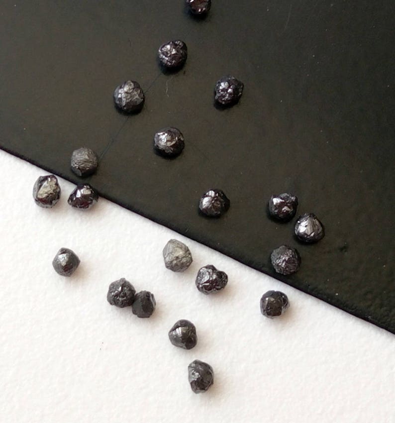 May include: A collection of black diamonds, some with a slight grey hue, scattered on a white and black surface. The diamonds are various sizes and shapes.