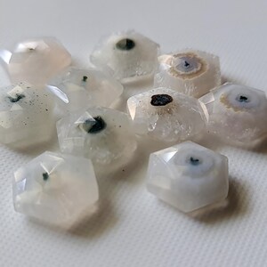 May include: A group of ten white agate stones with a variety of patterns and inclusions. The stones are all faceted and have a hexagonal shape.