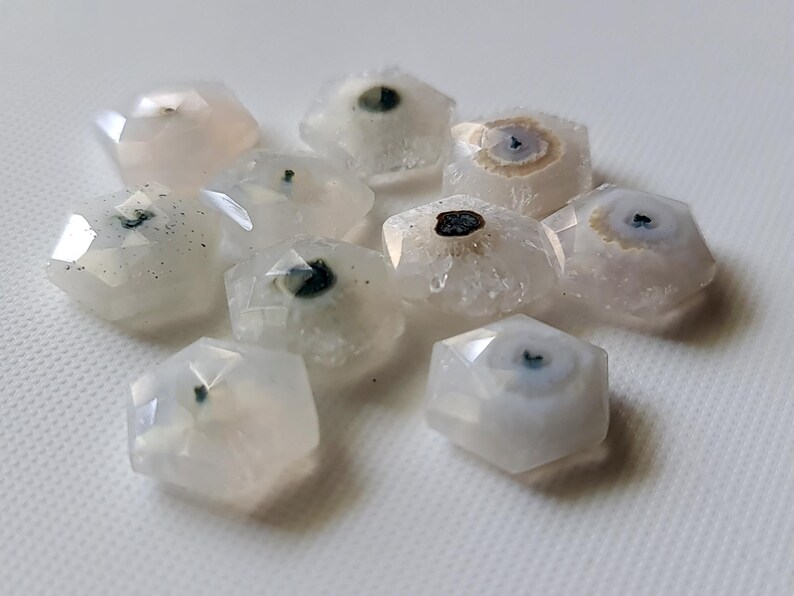 May include: A group of ten white agate stones with a variety of patterns and inclusions. The stones are all faceted and have a hexagonal shape.