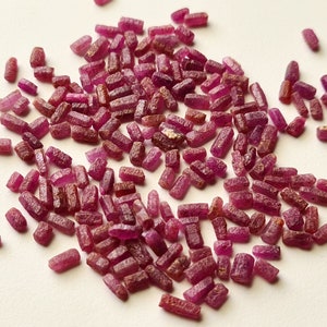 Peut inclure: Un grand tas de petites pierres précieuses de rubis rouges brutes. Les rubis sont tous de forme rectangulaire et ont une texture légèrement irrégulière.