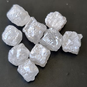Może przedstawiać: Grupa ośmiu surowych, białych, nieoszlifowanych diamentów. Diamenty są różnych rozmiarów i kształtów, niektóre mają bardziej sześcienny kształt, a inne są bardziej nieregularne.