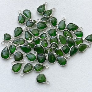 Puede incluir: Un grupo de 30 colgantes de piedra preciosa verde en forma de lágrima con anillos de salto de plata. Los colgantes son facetados y tienen un acabado brillante.