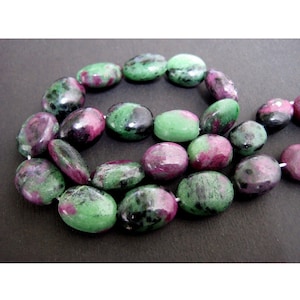 May include: A strand of oval-shaped green, pink, and black gemstone beads. The beads are strung on a clear thread.