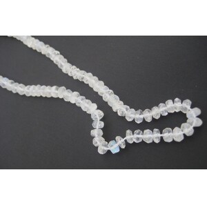 Peut inclure: Un collier de perles de pierre de lune blanche, chaque perle est facet&eacute;e et pr&eacute;sente une l&eacute;g&egrave;re qualit&eacute; iris&eacute;e.