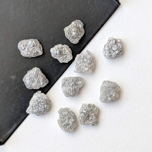 K&ouml;nnte beinhalten: Eine Sammlung von zehn rohen, grauen Diamanten. Die Diamanten sind in verschiedenen Gr&ouml;&szlig;en und Formen und haben ein nat&uuml;rliches, unpoliertes Aussehen.