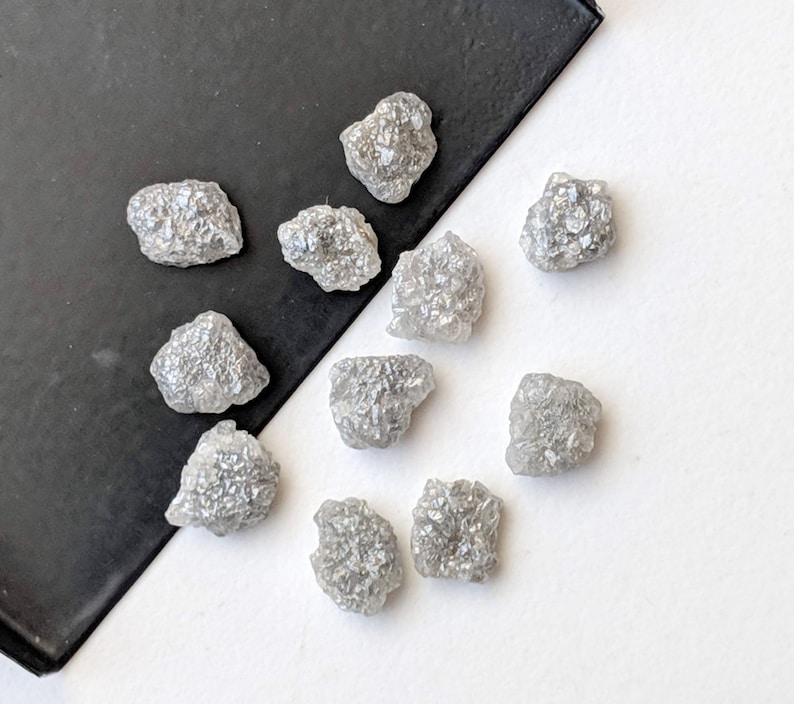 K&ouml;nnte beinhalten: Eine Sammlung von zehn rohen, grauen Diamanten. Die Diamanten sind in verschiedenen Gr&ouml;&szlig;en und Formen und haben ein nat&uuml;rliches, unpoliertes Aussehen.