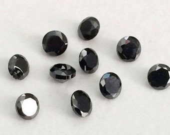 May include: Ten black round gemstones with a faceted cut. The gemstones are arranged in a scattered pattern on a white surface.