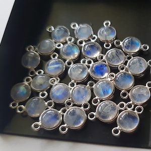 May include: A group of 20 silver-toned gemstone connectors with a round, iridescent moonstone cabochon. Each connector has two loops for attaching to jewelry.