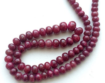 May include: A strand of deep red ruby beads, each bead is smooth and round, with a slightly irregular shape. The beads are strung together on a clear thread.