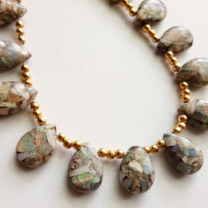 May include: A gold chain necklace with teardrop-shaped opal beads. The beads are a mix of green, brown, and white.