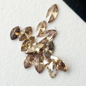 May include: A group of marquise-shaped brown diamonds, some with a more golden hue, arranged on a white surface.