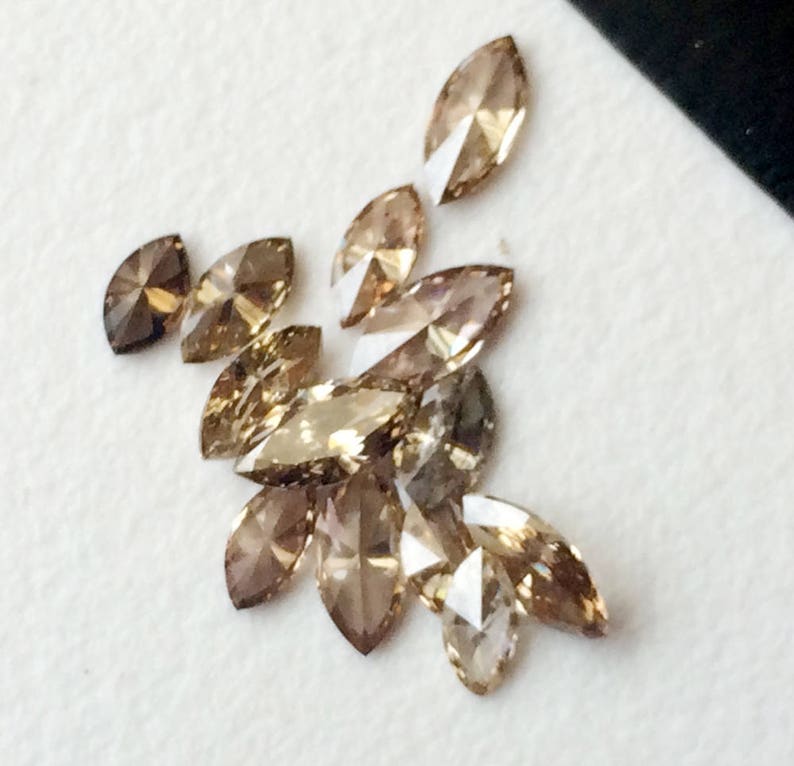 May include: A group of marquise-shaped brown diamonds, some with a more golden hue, arranged on a white surface.