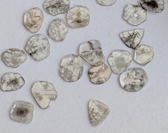May include: A collection of rough, grey diamonds with a variety of shapes and sizes. The diamonds have a cloudy, translucent appearance.
